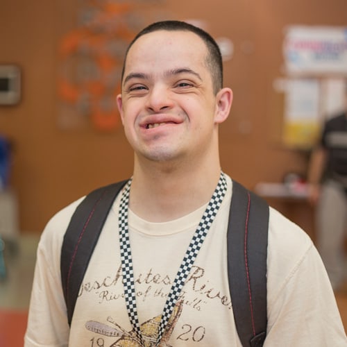 Man standing in a classroom with a backpack on.