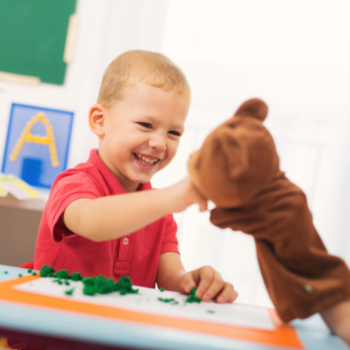 Child smiling and playing with bear puppet.
