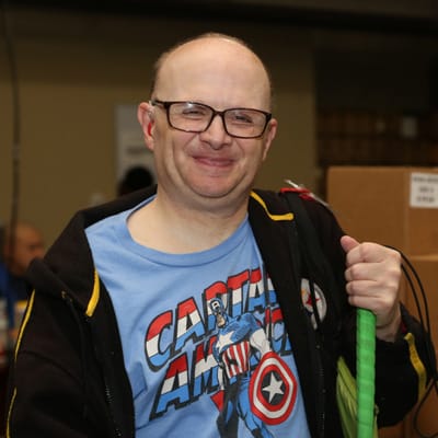 Man in a black jacket an blue shirt holding a walking cane.