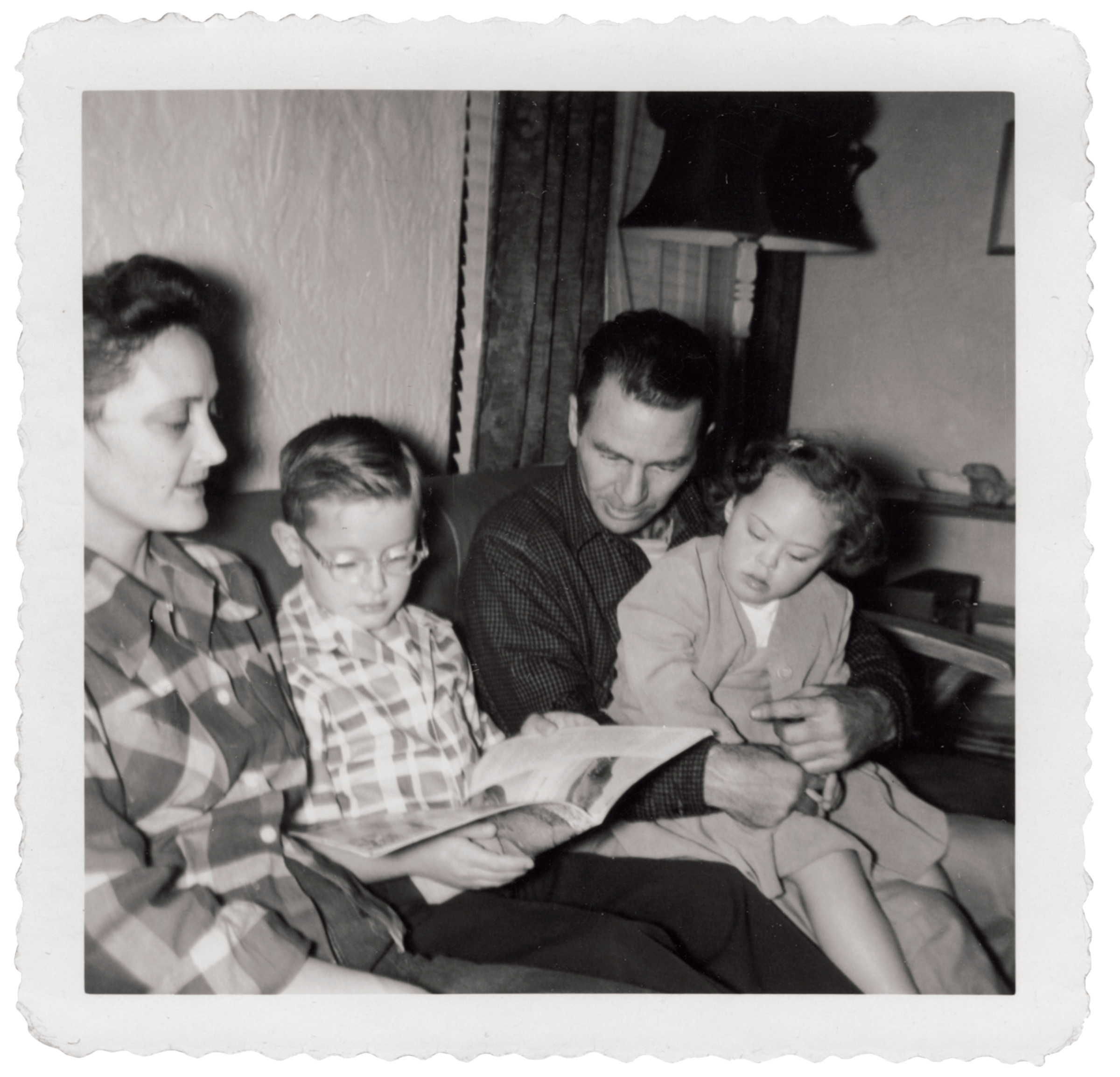 Family of two adults and two children sitting on a couch reading together.