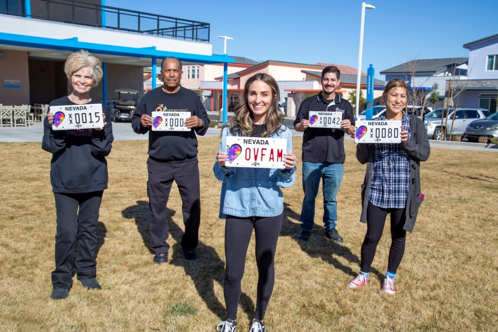 People standing outside holding personalized charity license plates.