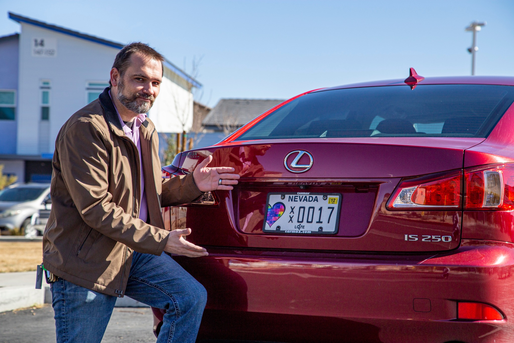 Man crouching down next to red car with personalized license plate.