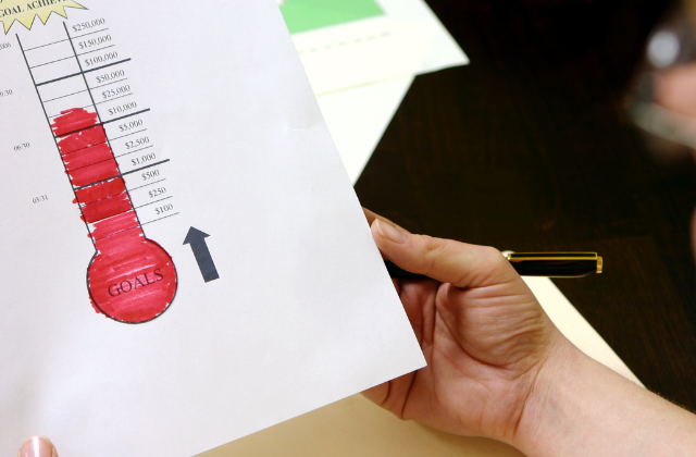 school-fundraising-ideas-feature Person holding a piece of paper used for fundraising goal tracking.