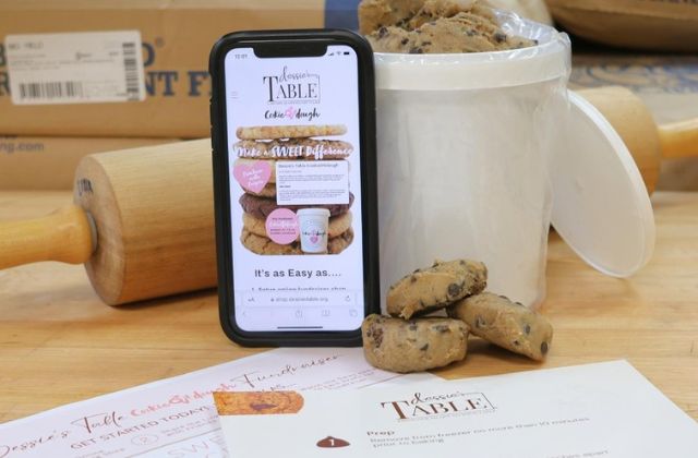 cell phone resting against a white pail of cookies on a wood table with a rolling pin in the background
