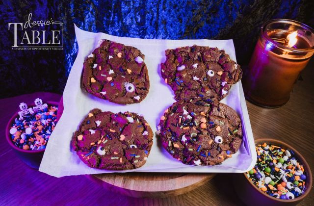 four chocolate cookies on a platter with sprinkles and a candle on the table set for a spooky theme