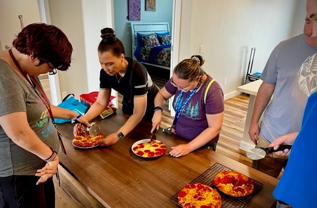 Woman showing adults with disabilities how to cut pizza slices.