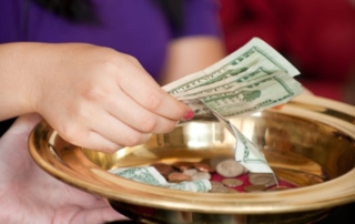 Hand setting money into an offering dish at church.