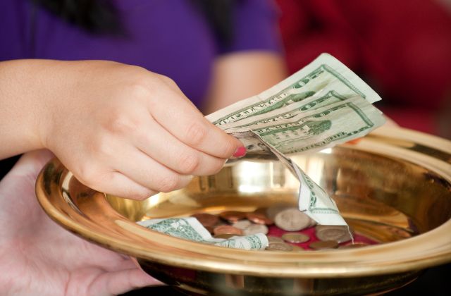 Hand setting money into an offering dish at church.