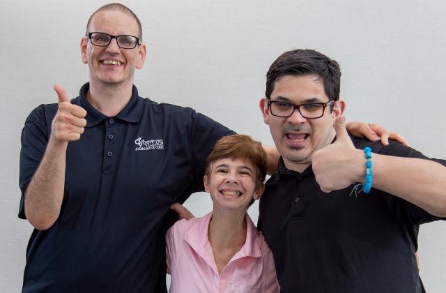 Three people with their arms around each other giving a thumbs up sign.