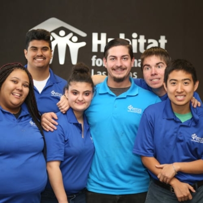 Six people in blue shirts standing in front of a Habitat for Humanity logo sign.