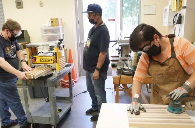 Two people working on woodworking projects while another observes.