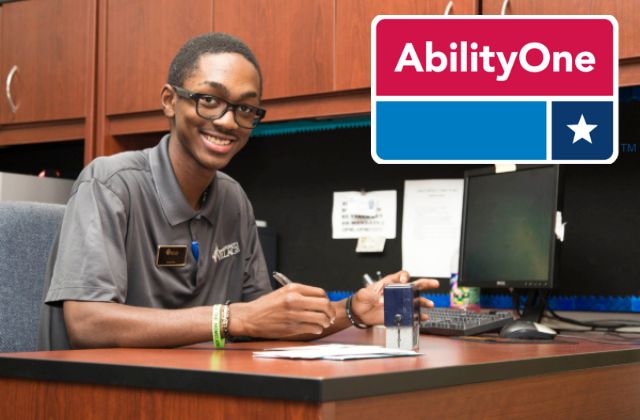 Man sitting at office desk with an AbilityOne logo to the side of the image.
