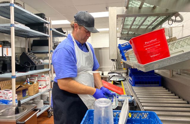 Man washing dishes in a commercial kitchen.