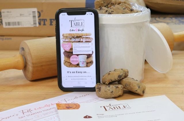 Mobile phone next to a white pail full of cookies on a bakers wooden table.