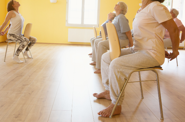 Adults in a room practicing chair yoga.