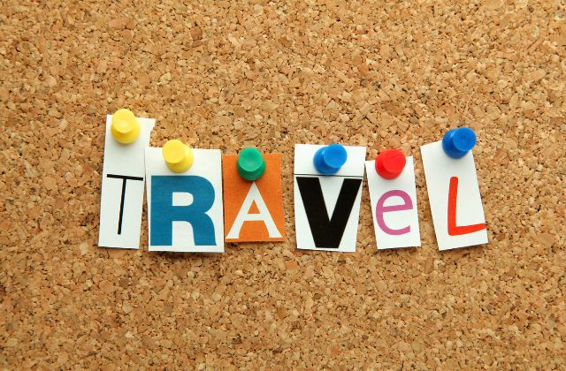 Cork board with individual pieces of paper tacked by pushpins spelling the word "travel".