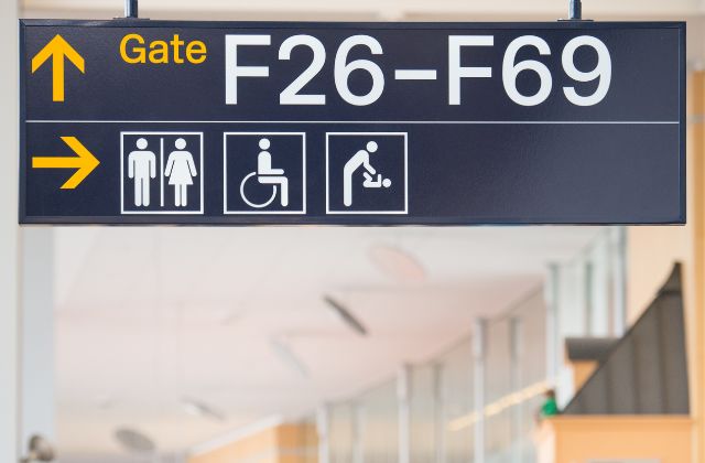 Gate signs at an airport with yellow arrows pointing to different illustrated services for restrooms and changing rooms.