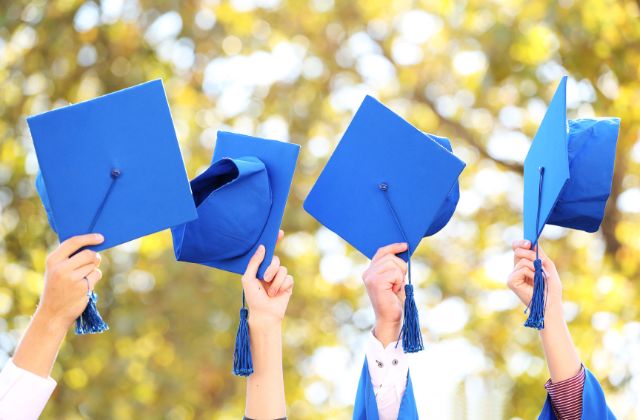 four blue graduation caps held in the air with trees in the background