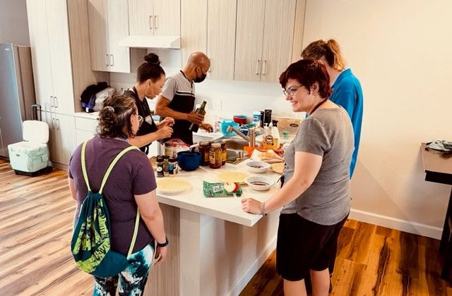 group of adults standing around a kitchen counter making pizza