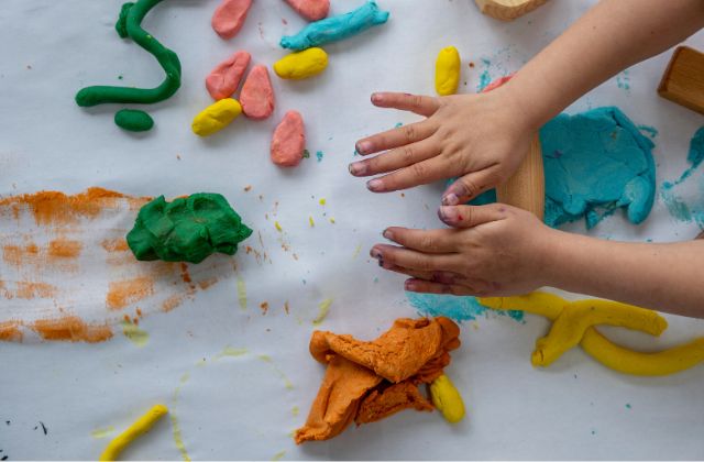 two hands rolling colored dough on a table.