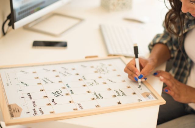 woman writing on a large erasable calendar board