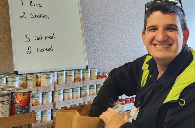 young man filling a brown bag with canned food