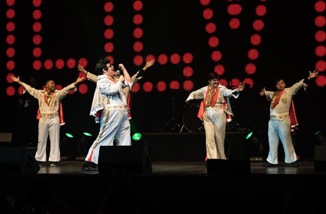 group of four elvis impersonators on stage singing and dancing