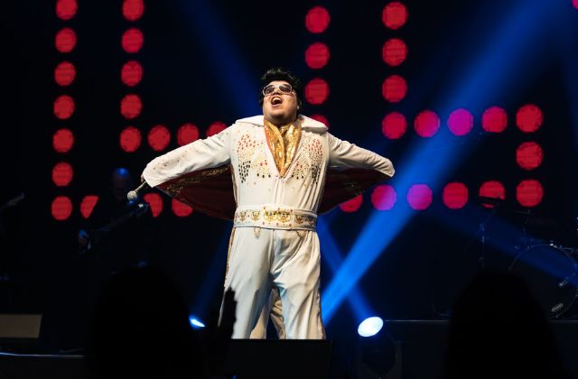 elvis impersonator dressed in white on stage at a performance