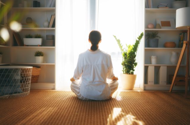 back view of woman meditation on the floor in front of a window.