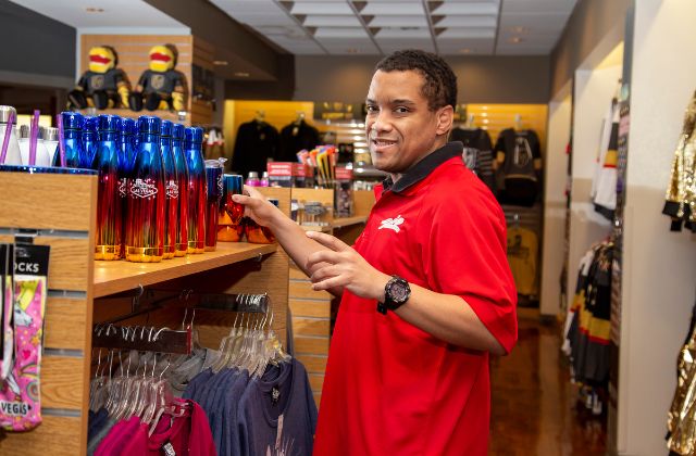 man in a red shirt standing next to a retail counter of water bottles and shirts