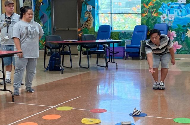 three people playing bean bag toss game indoors