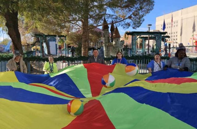 group of people holding a large, colorful piece of fabric to bounce a ball.