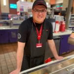 person in a worker's uniform standing behind a popcorn machine