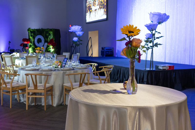 several white clothed tables with flower arrangements in vases at an event venue