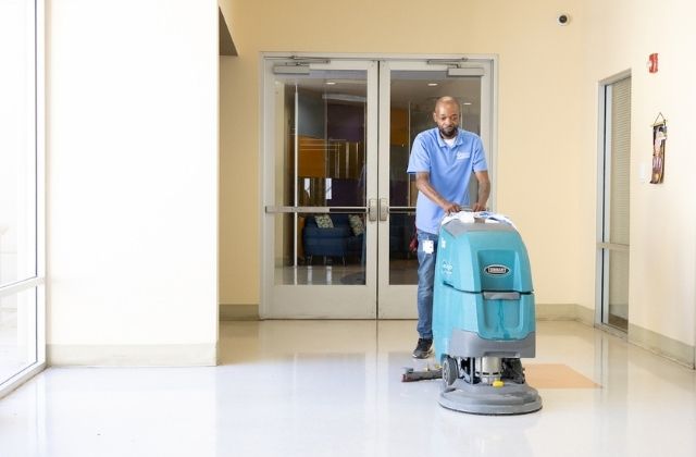 person pushing a commercial floor cleaner in the hallway of an office building