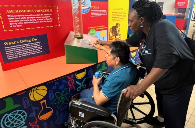 person standing helping another person seated at a science exhibit