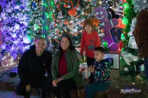 A family of four poses together surrounded by brightly lit Christmas trees and holiday decorations at the Magical Forest.